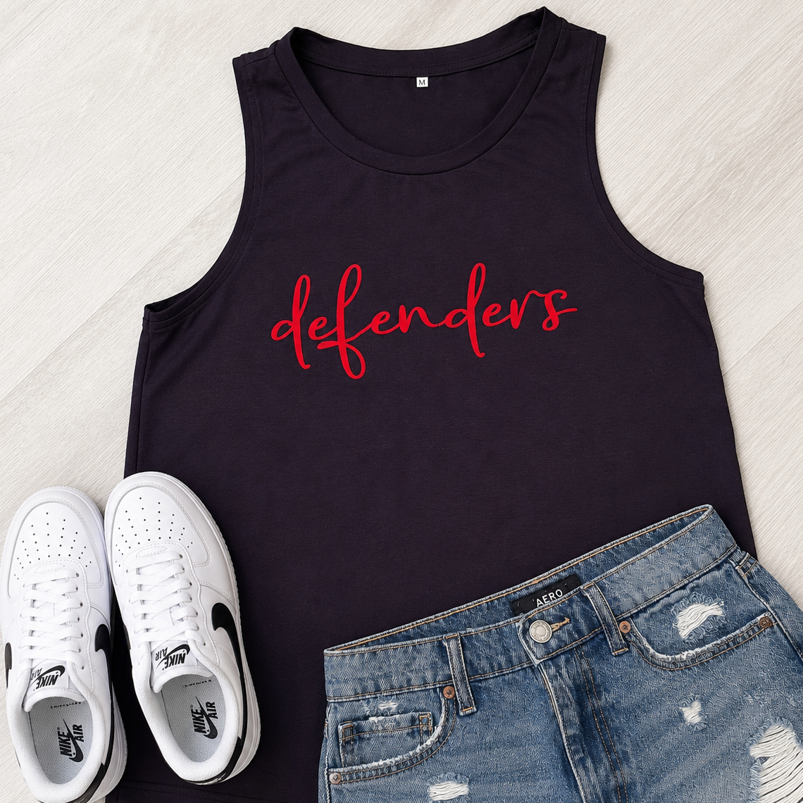 A black sleeveless tank top with the word 'defenders' printed in red script across the chest, styled in a flat lay with white sneakers and distressed blue denim shorts on a light wood background.