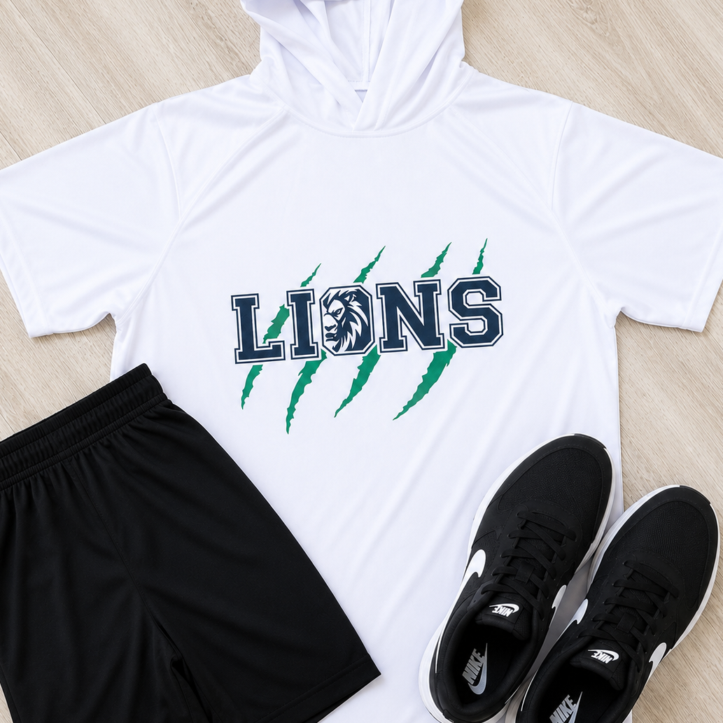 A flat-lay athletic outfit on a light wood floor featuring a white short-sleeve hooded shirt with 'LIONS' and green claw graphics, black athletic shorts with a white Under Armour logo, and black Nike sneakers.