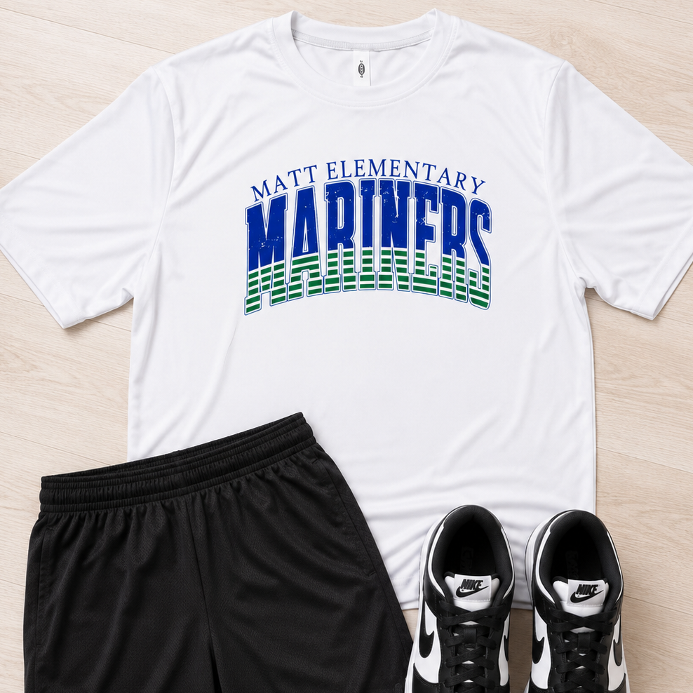 A flat-lay outfit consisting of a white short-sleeve graphic T-shirt with 'MATT ELEMENTARY MARINERS' in blue and green, black athletic shorts, and black-and-white Nike sneakers, arranged on a light wood floor.