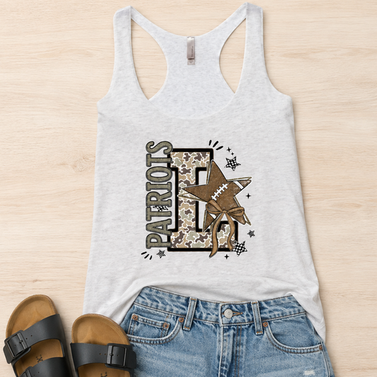 A flat-lay outfit arrangement featuring a light gray racerback tank top with a 'Patriots FF' graphic, paired with denim shorts and black slide sandals on a light wood background.