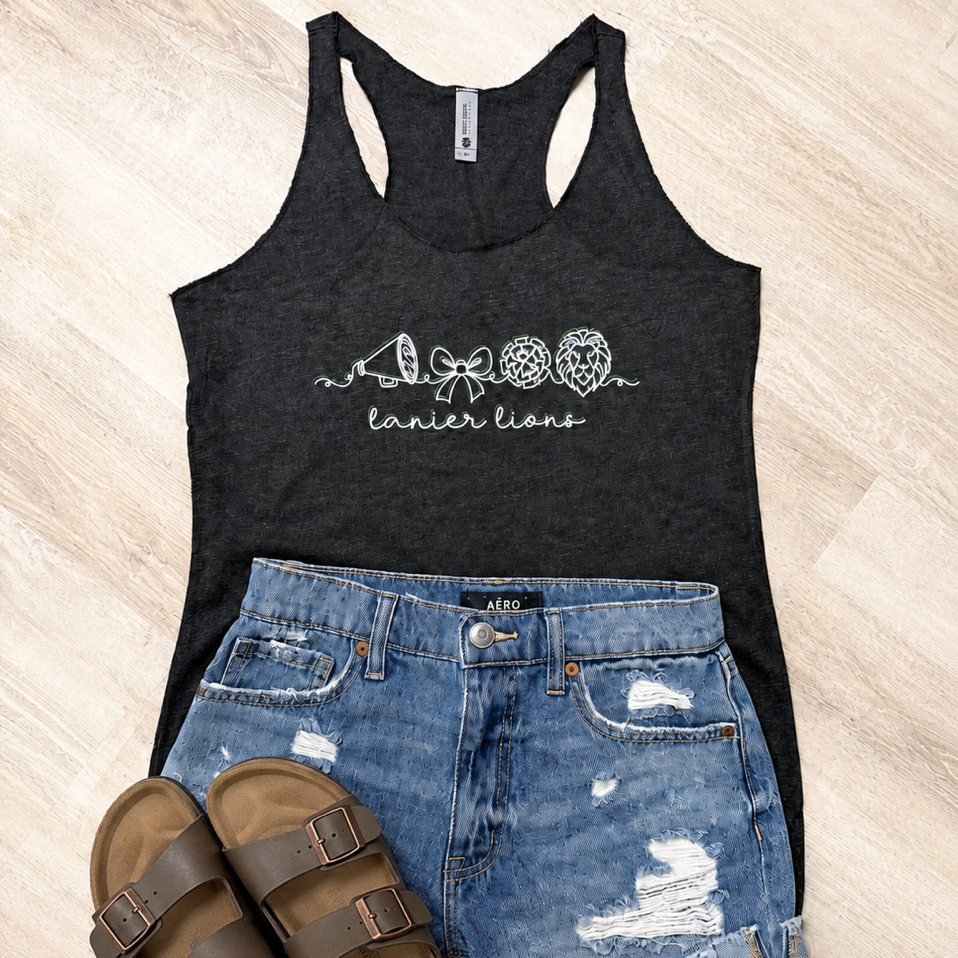 A flat-lay of a women's black racerback tank top with a white 'lancer lions' graphic, paired with distressed blue denim shorts and brown slide sandals on a light wood floor background.