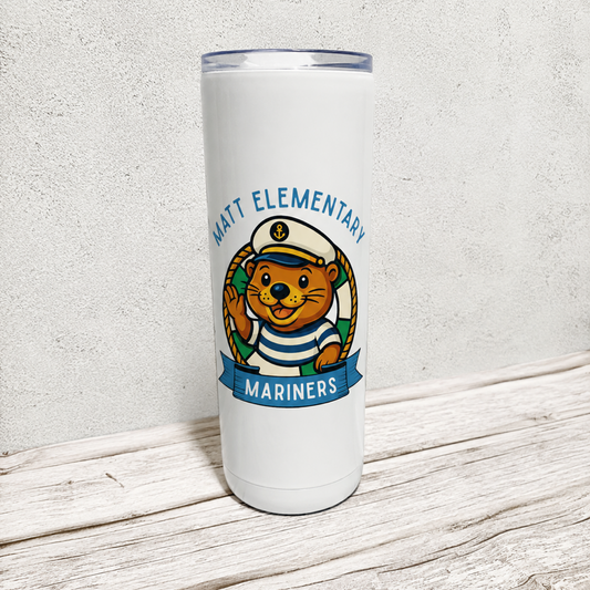 A white insulated travel tumbler with a clear lid, featuring a cartoon beaver mascot wearing a sailor hat and striped shirt, with the text 'MATT ELEMENTARY MARINERS' printed on the front. The tumbler is photographed standing on a rustic white wooden surface against a textured light gray wall.