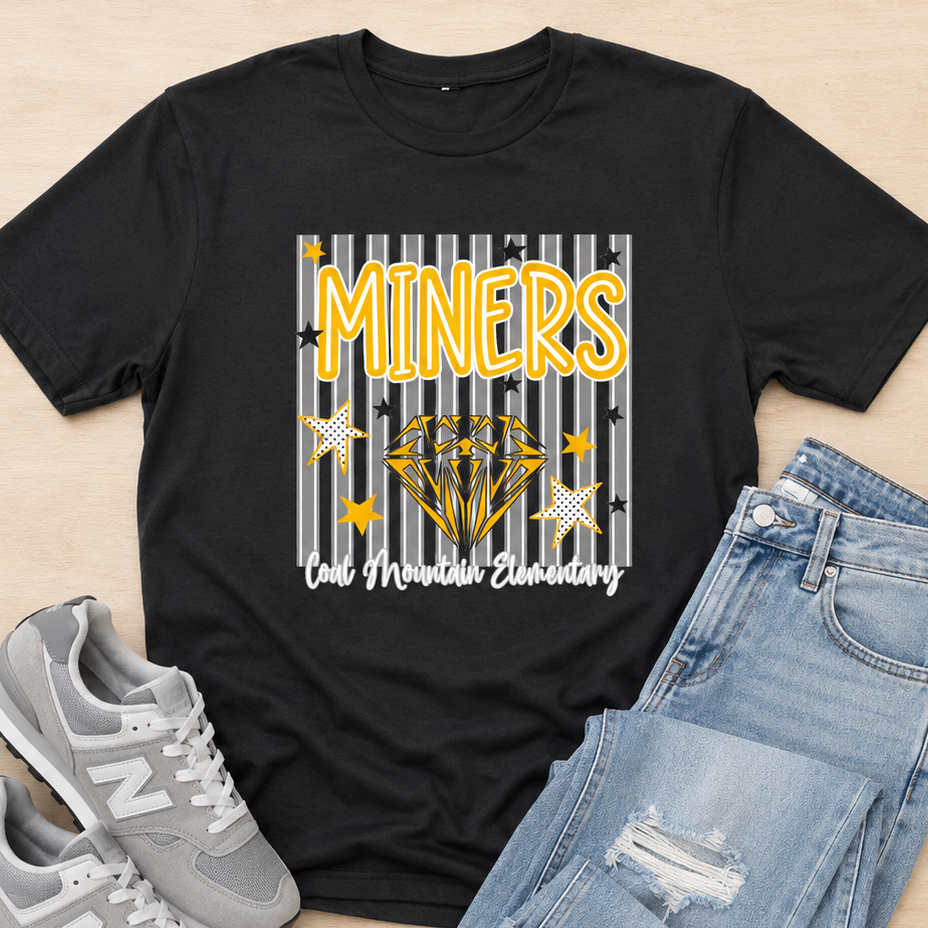 A black graphic t-shirt featuring a 'MINERS Cal Mineral Academy' design with a diamond illustration, styled in a flat lay with light blue jeans and gray New Balance sneakers on a light wood background.