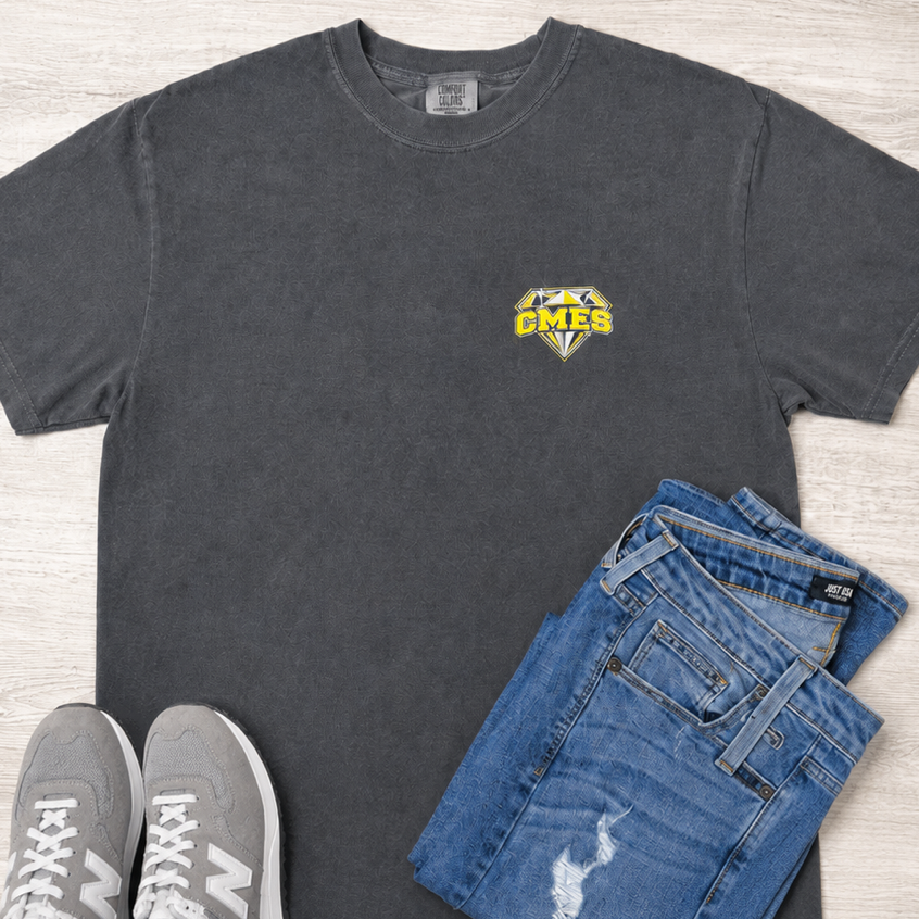A dark gray crewneck t-shirt with a yellow and blue 'PUBG' chest graphic, styled in a flat lay with blue jeans and gray New Balance sneakers on a light wood background.