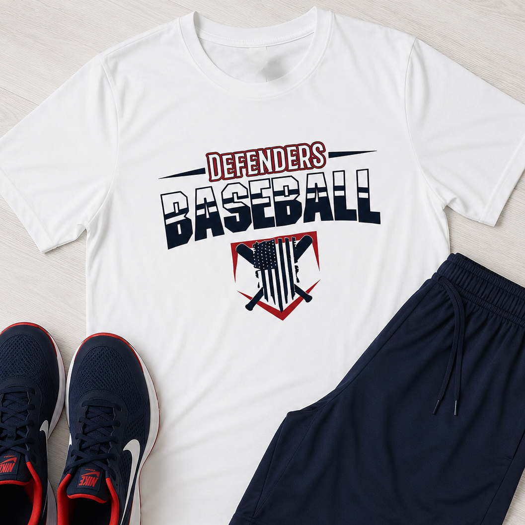 A flat-lay of a white graphic T-shirt with navy and red 'Defenders Baseball' text and a shield logo, paired with navy athletic shorts and navy sneakers on a light wood background.