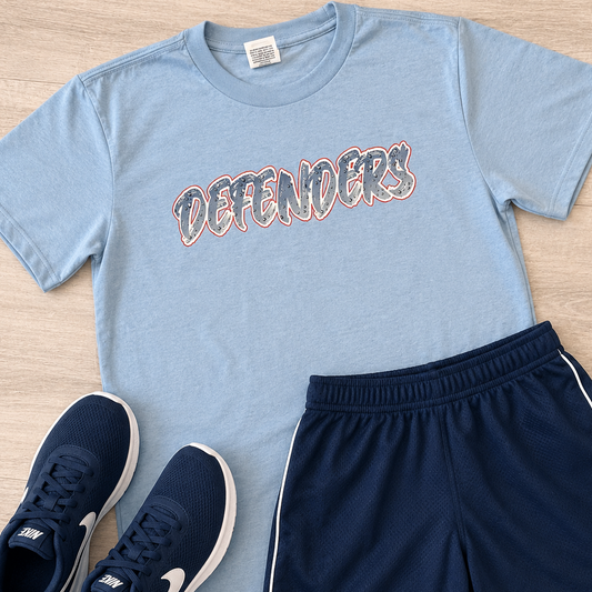 A kids' athletic outfit set featuring a light blue t-shirt with 'DEFENDERS' printed across the chest, navy blue athletic shorts with white side stripes, and a pair of navy blue sneakers, all arranged on a light wood background.
