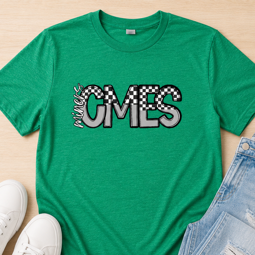 A green graphic t-shirt with 'OMES' in a zebra-print and checkered font, styled in a flat lay with white sneakers and distressed light blue jeans on a light wood background.
