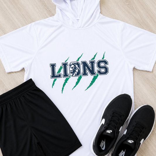 A flat-lay athletic outfit on a light wood floor featuring a white short-sleeve hooded shirt with 'LIONS' and green claw graphics, black athletic shorts with a white Under Armour logo, and black Nike sneakers.