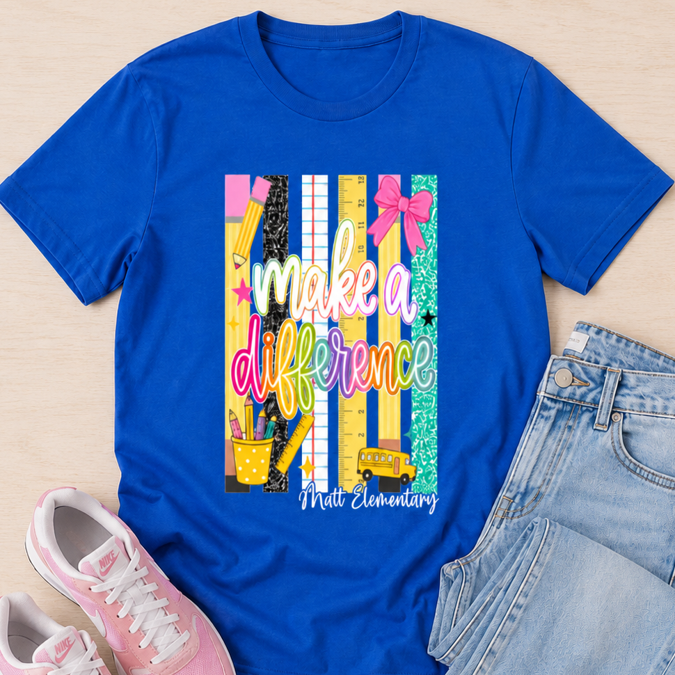 A flat-lay outfit arrangement featuring a royal blue short-sleeve graphic T-shirt with the text 'make a difference' and 'Medi Elementary' over a colorful striped chalkboard design, styled with light-wash jeans and pink sneakers on a light wood background.