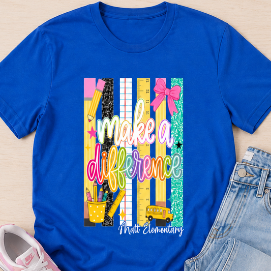 A flat-lay outfit arrangement featuring a royal blue short-sleeve graphic T-shirt with the text 'make a difference' and 'Medi Elementary' over a colorful striped chalkboard design, styled with light-wash jeans and pink sneakers on a light wood background.