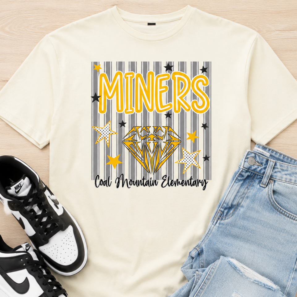An off-white graphic t-shirt featuring a 'Miners' school pride design with a striped background, yellow diamond, and black text, styled in a flat lay with light blue jeans and black-and-white sneakers on a light wood background.