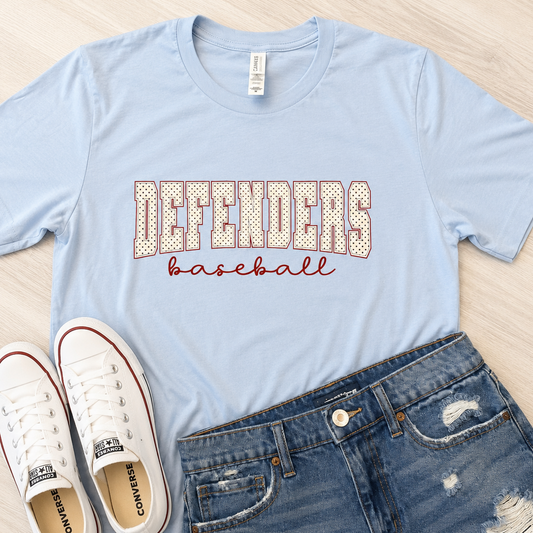A light blue graphic t-shirt with 'DEFENDERS baseball' printed on the front, styled in a flat lay with white Converse sneakers and distressed blue jeans on a light wood background.