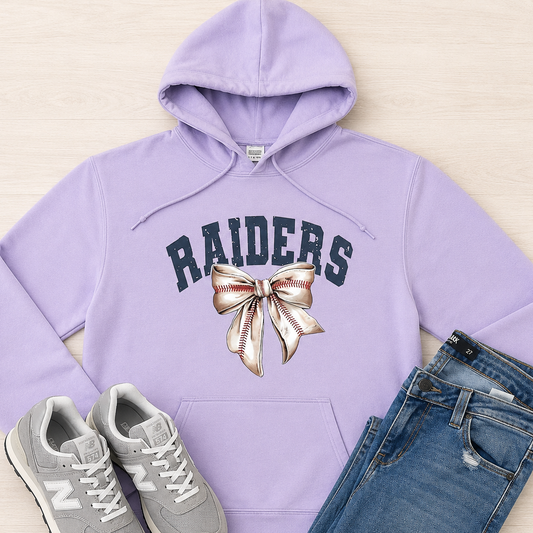 A lavender purple hoodie with 'RAIDERS' and a baseball bow graphic, styled in a flat lay with gray New Balance sneakers and blue jeans on a light wood background.