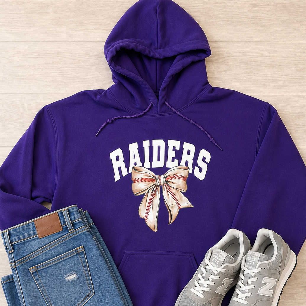 A purple hoodie with 'RAIDERS' and a baseball bow graphic, styled in a flat lay with blue jeans and gray New Balance sneakers on a light wood background.