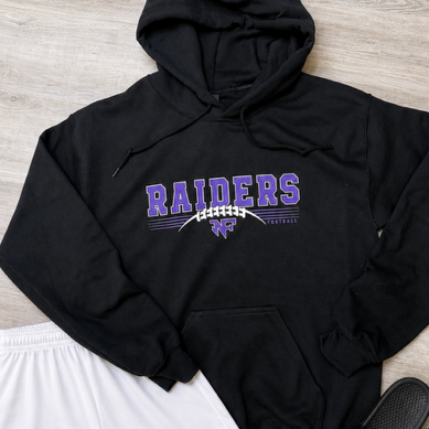A black pullover hoodie with purple and white 'RAIDERS' lettering across the chest, styled in a flat lay with white athletic shorts and black slide sandals on a light wood floor.