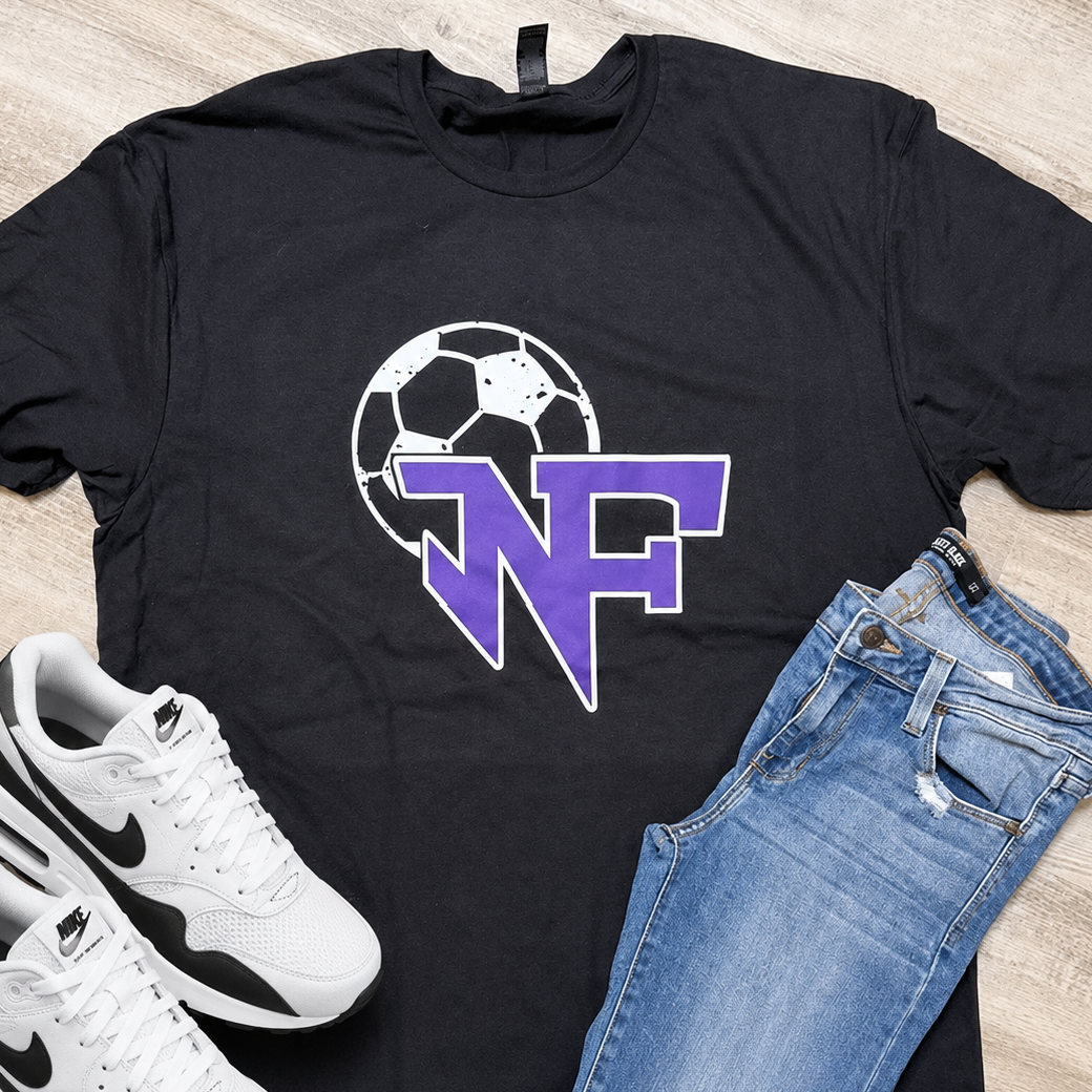 A black graphic t-shirt with a purple and white 'NF' logo over a soccer ball, styled in a flat lay with blue jeans and white Nike sneakers on a light wood floor.