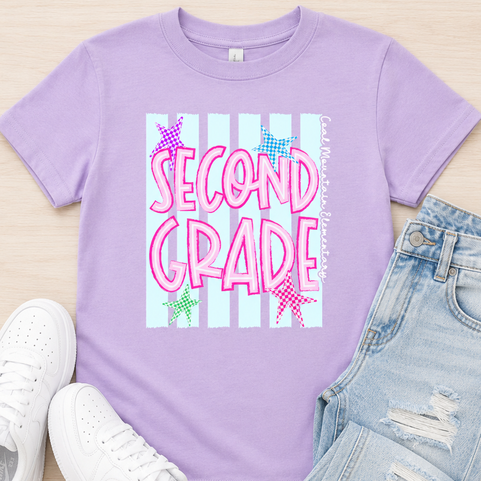 A flat-lay of a lavender purple t-shirt with a 'SECOND GRADE' graphic, styled with light-wash distressed denim jeans and white sneakers on a light wood background.