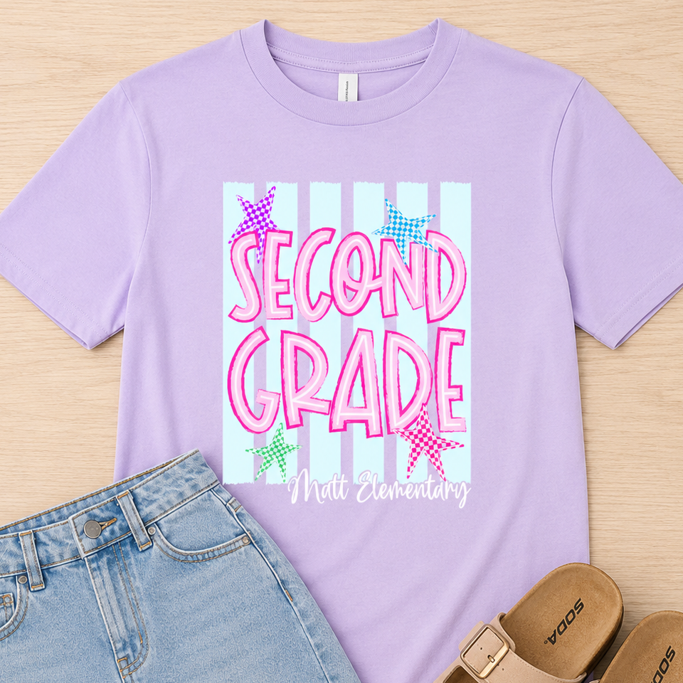 A flat-lay outfit featuring a light purple t-shirt with a 'Second Grade Mill Elementary' graphic, paired with a light blue denim skirt and tan slide sandals on a light wood background.